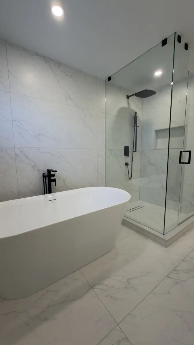 Rustic wood-tile corner shower and oak vanity replaced with a marble walk-in shower, freestanding tub and sage double vanity — after