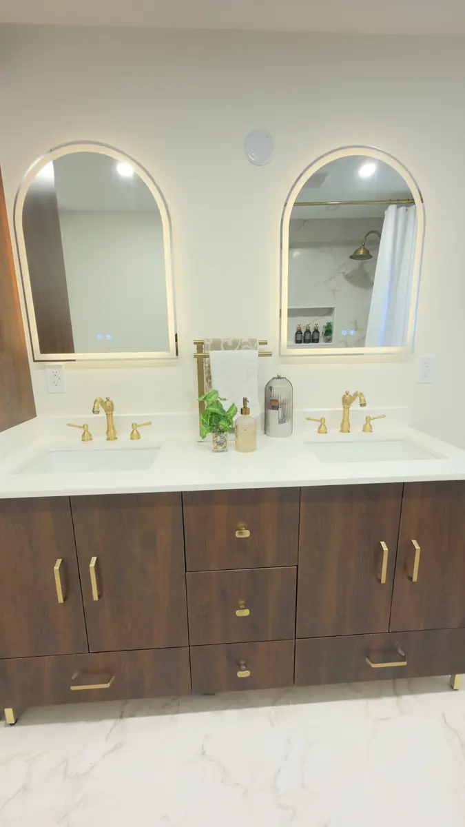 Dated lilac-tiled bathroom with a white builder vanity rebuilt with a walnut double vanity, gold fixtures and arched mirrors — after
