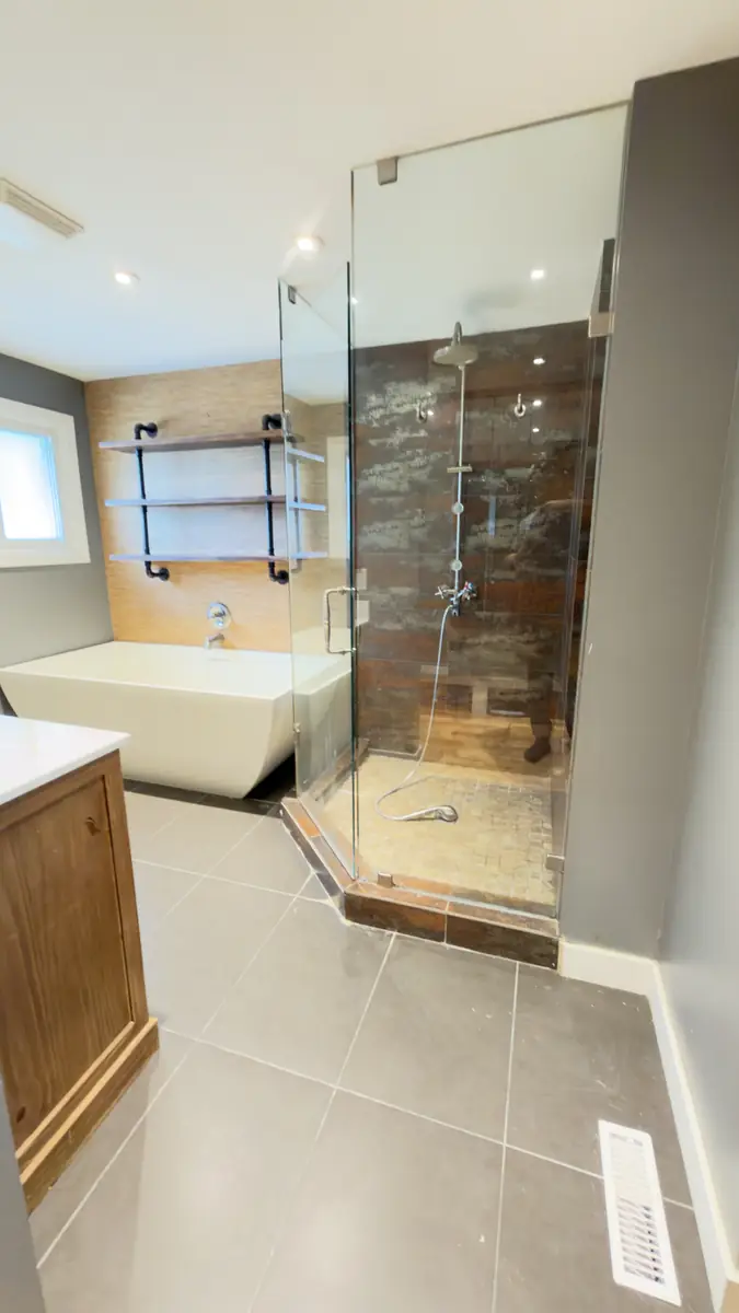 Rustic wood-tile corner shower and oak vanity replaced with a marble walk-in shower, freestanding tub and sage double vanity — before