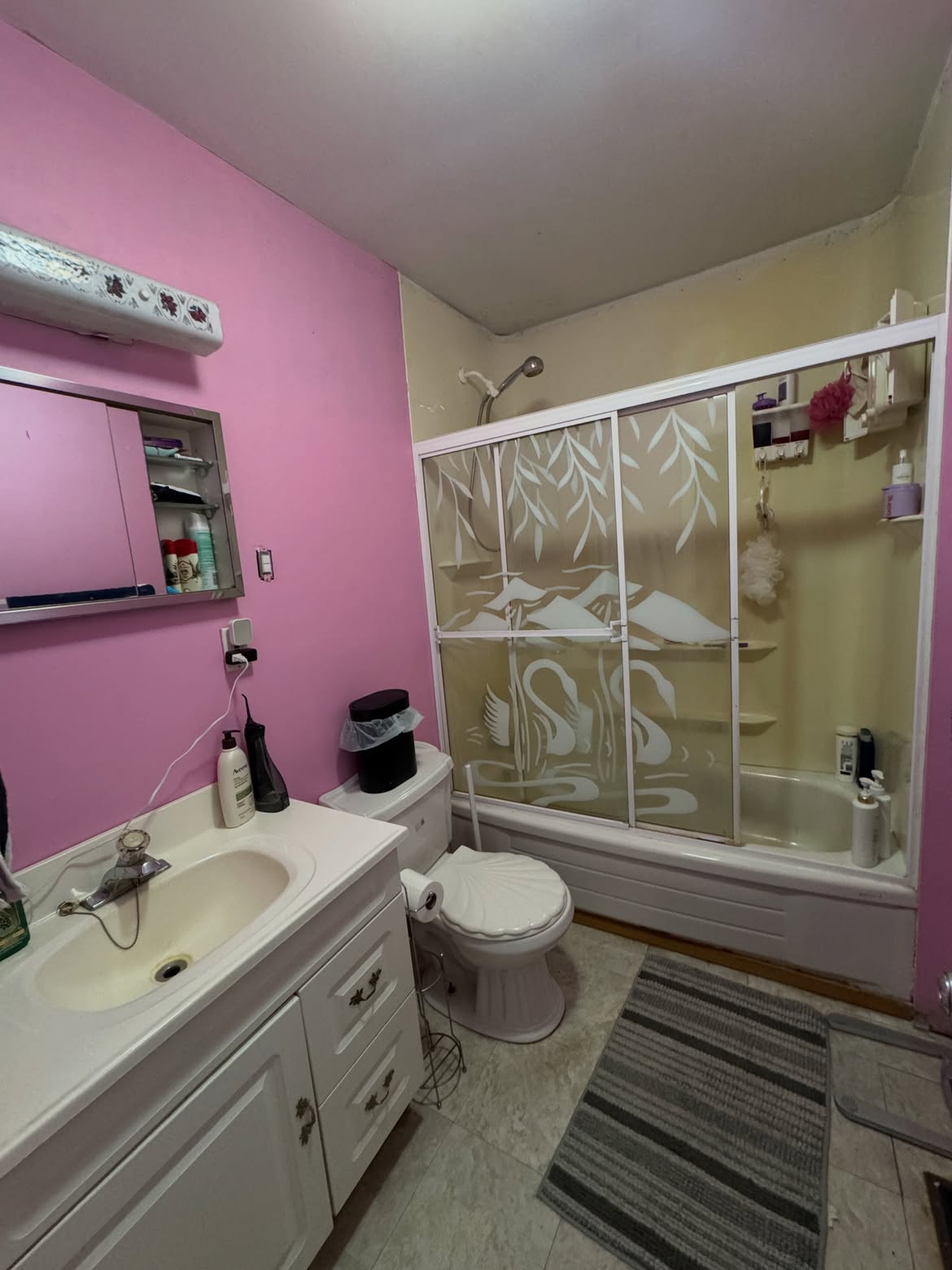 Dated pink bathroom replaced with white marble tile and a walk-in shower — before